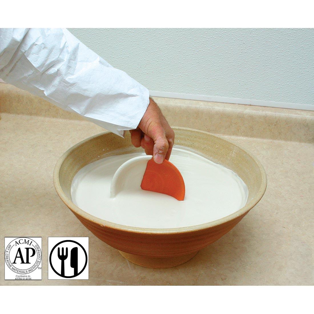 pottery being dipped into a bowl of AMACO Clear Low Fire Dipping Glaze, with AP Seal and food safe symbols