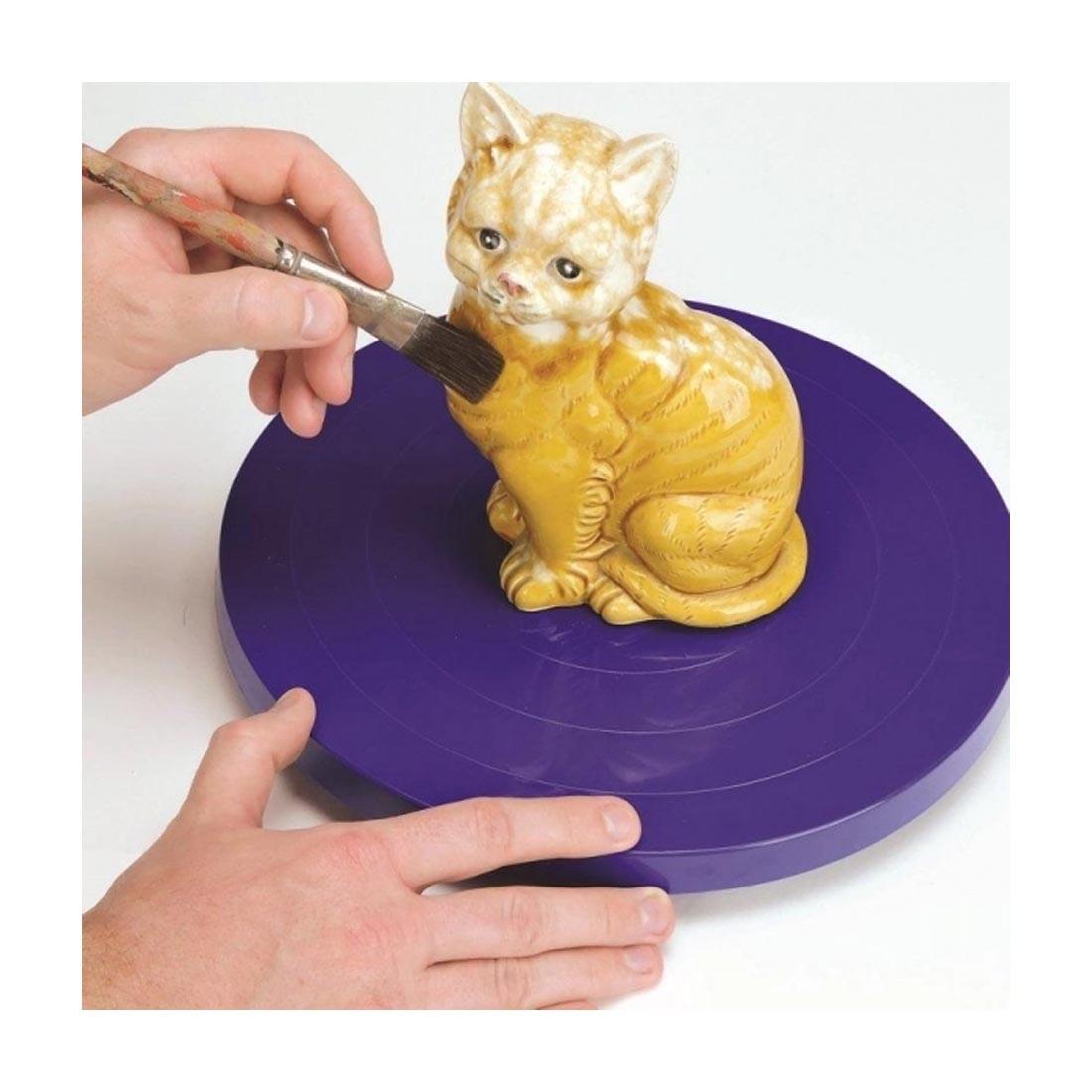 Hands using the Activa 10" Sculpting Wheel to glaze a cat statue