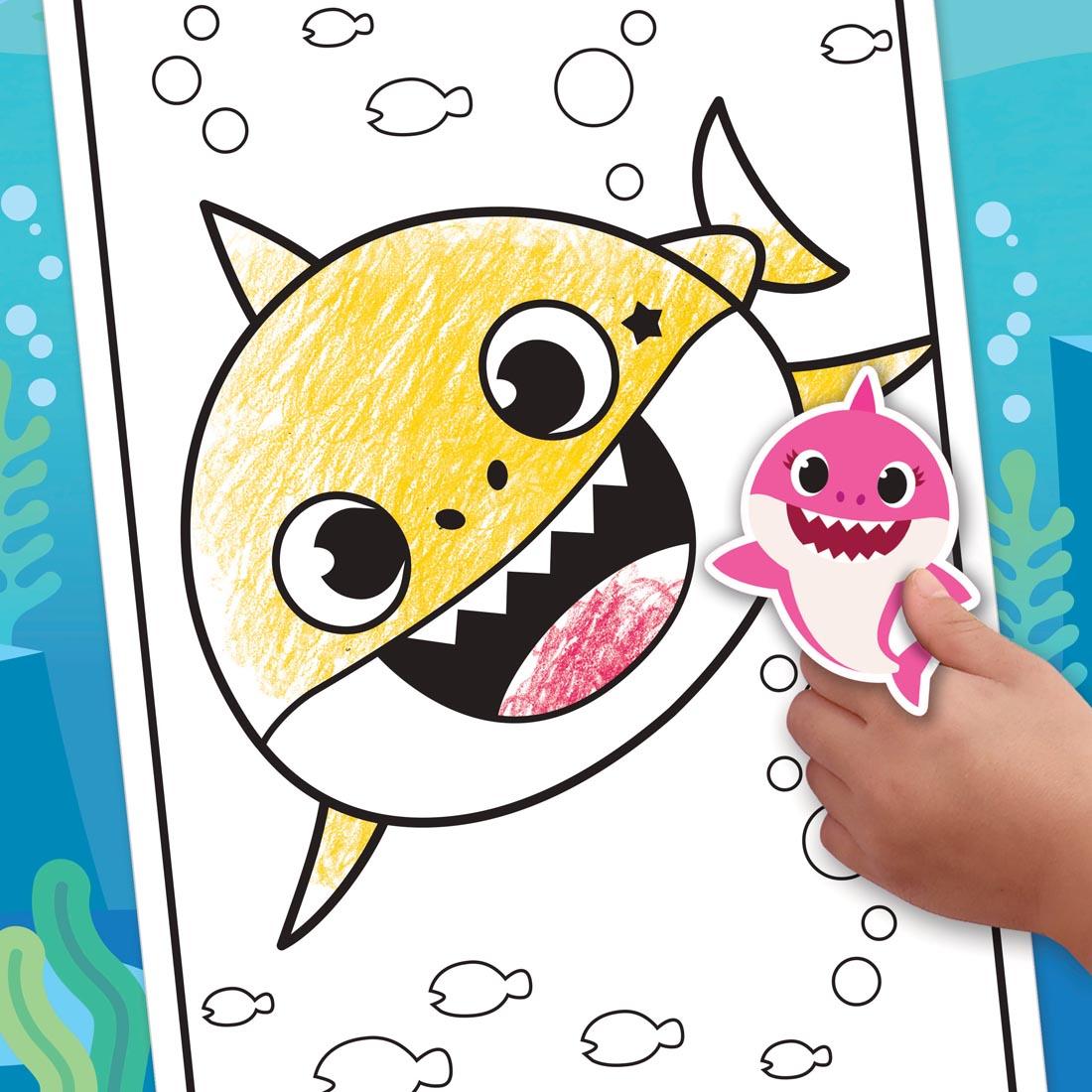 hand holding a sticker over a colored page from the Crayola Baby Shark Coloring Book