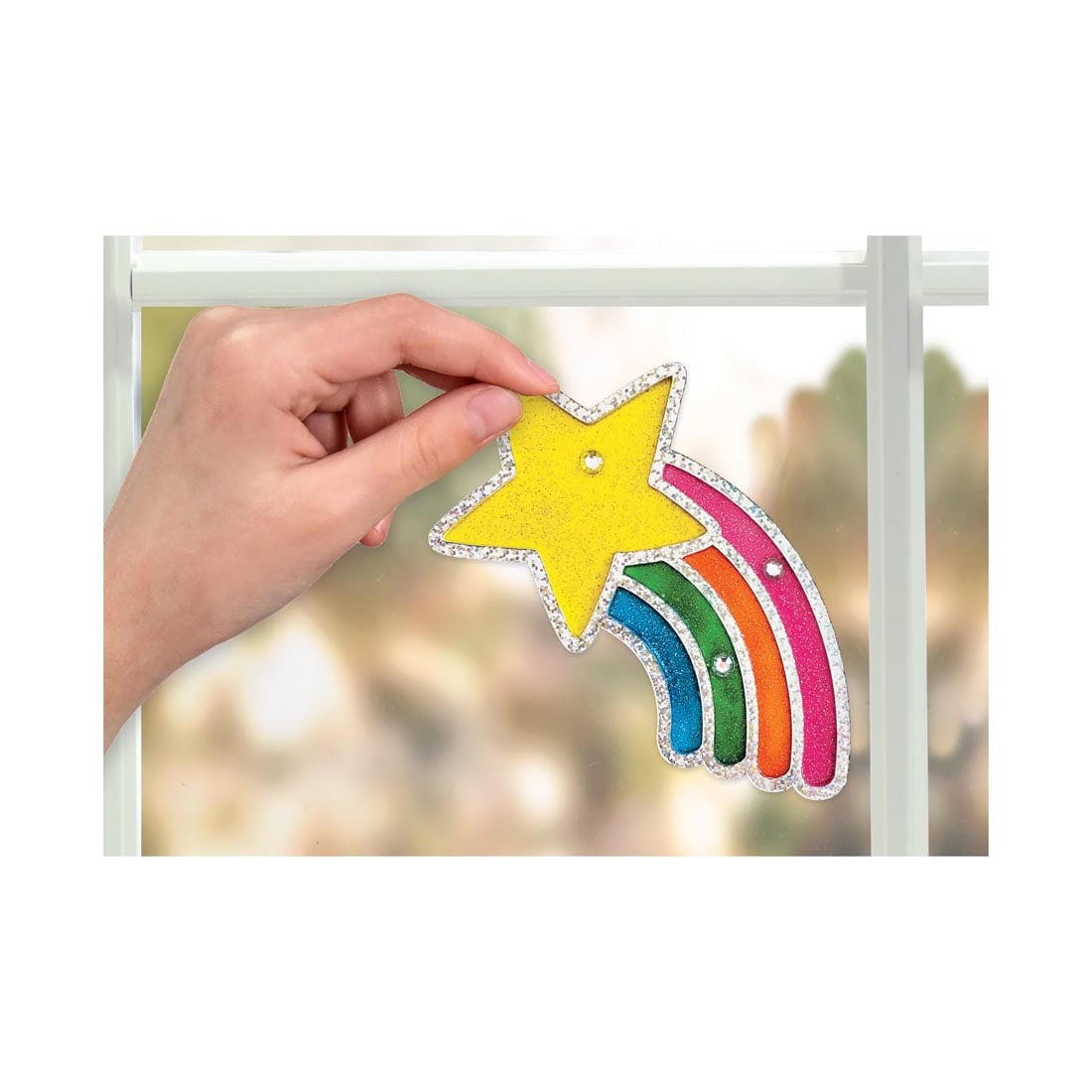 hand applying a completed shooting star from the Easy Sparkle Window Art By Creativity For Kids to a window