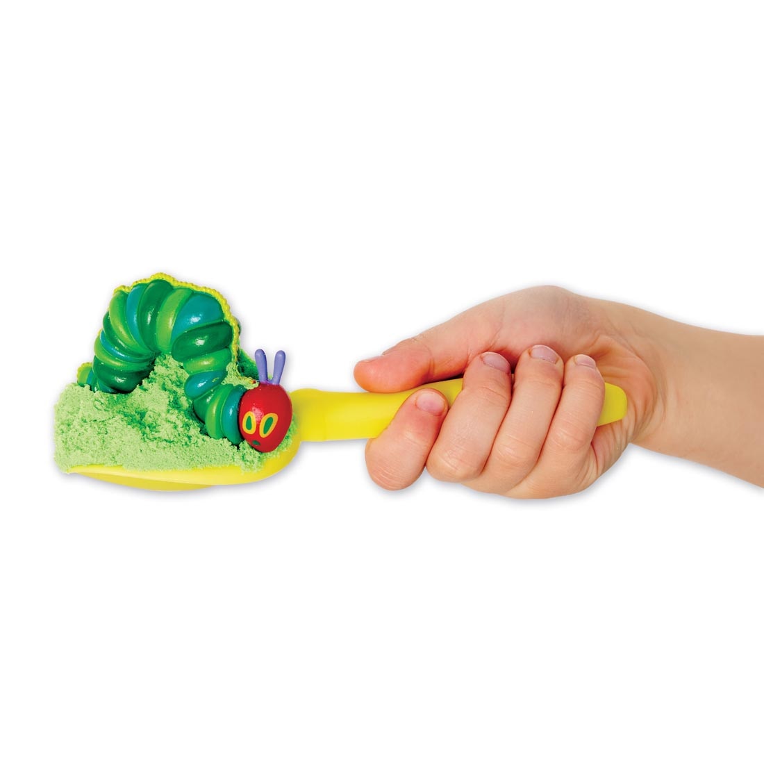 hand holding a shovel, which has sand and the Very Hungry Caterpillar figurine inside