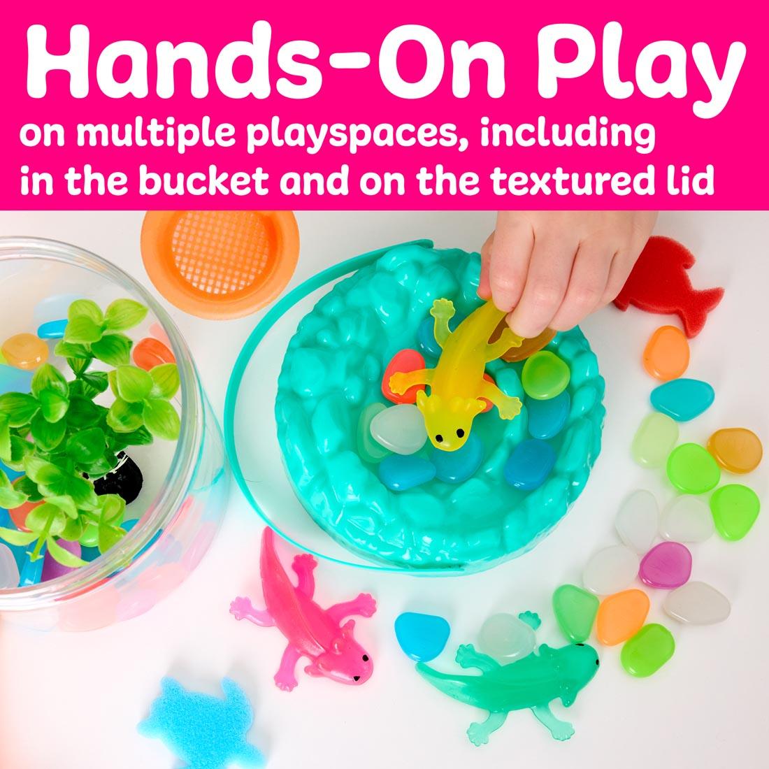 Hand playing with Axolotls Sensory Adventure Water Play set, with the words: Hands-On Play on multiple playspaces, including in the bucket and on the textured lid