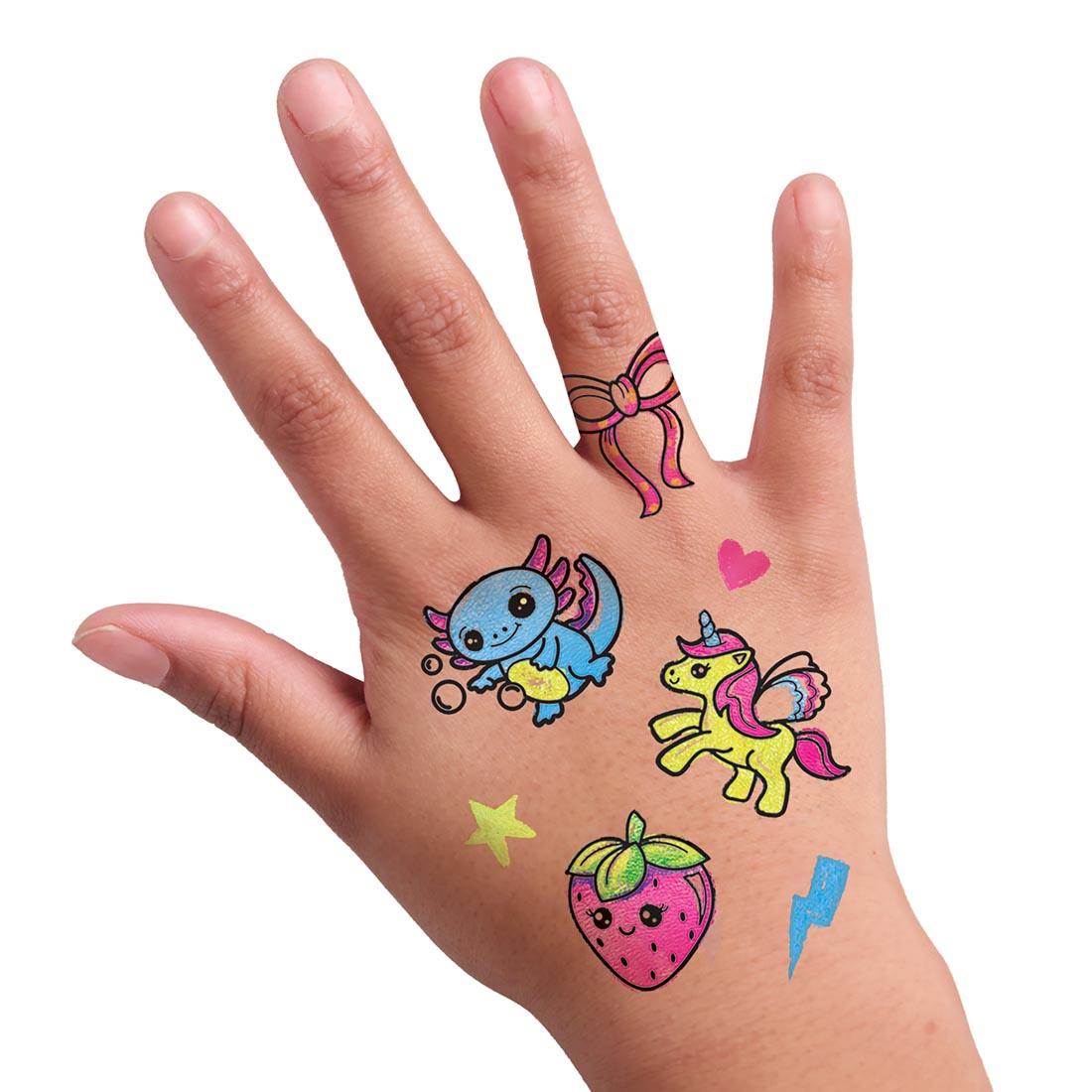 hand with several colorful tattoos, showing an axolotl, unicorn, strawberry and more