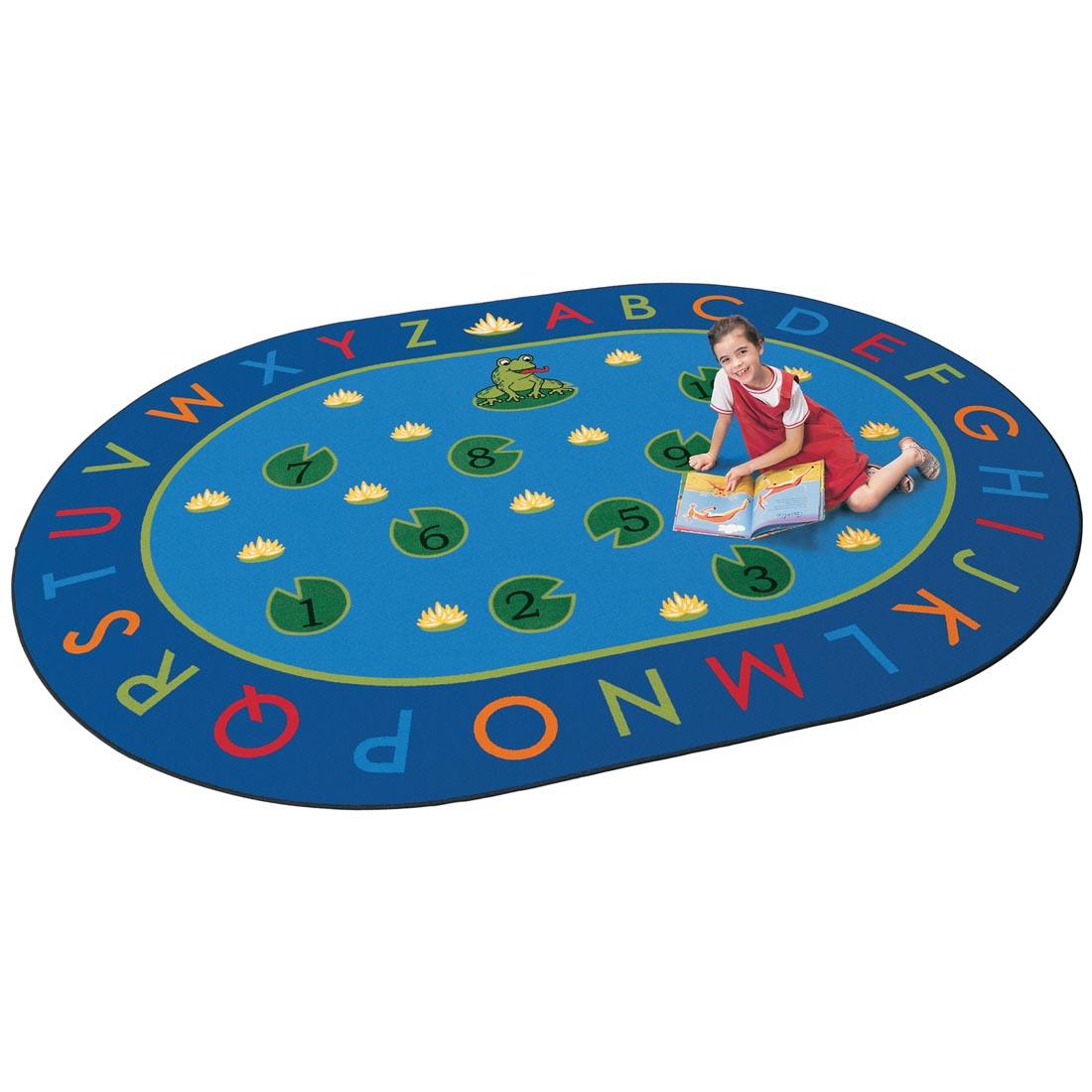 Child with a book sitting on the Frog-Themed Hip Hop to the Top Oval Rug by Carpets For Kids