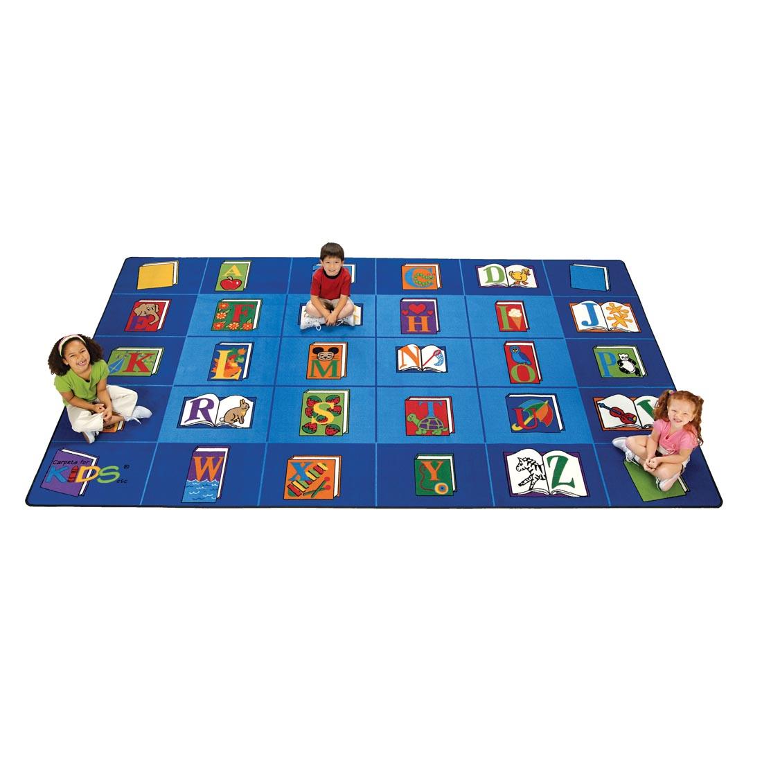 Rectangle Rug by Carpets For Kids, where each alphabet letter is shown on a book cover; 3 children are sitting on the rug