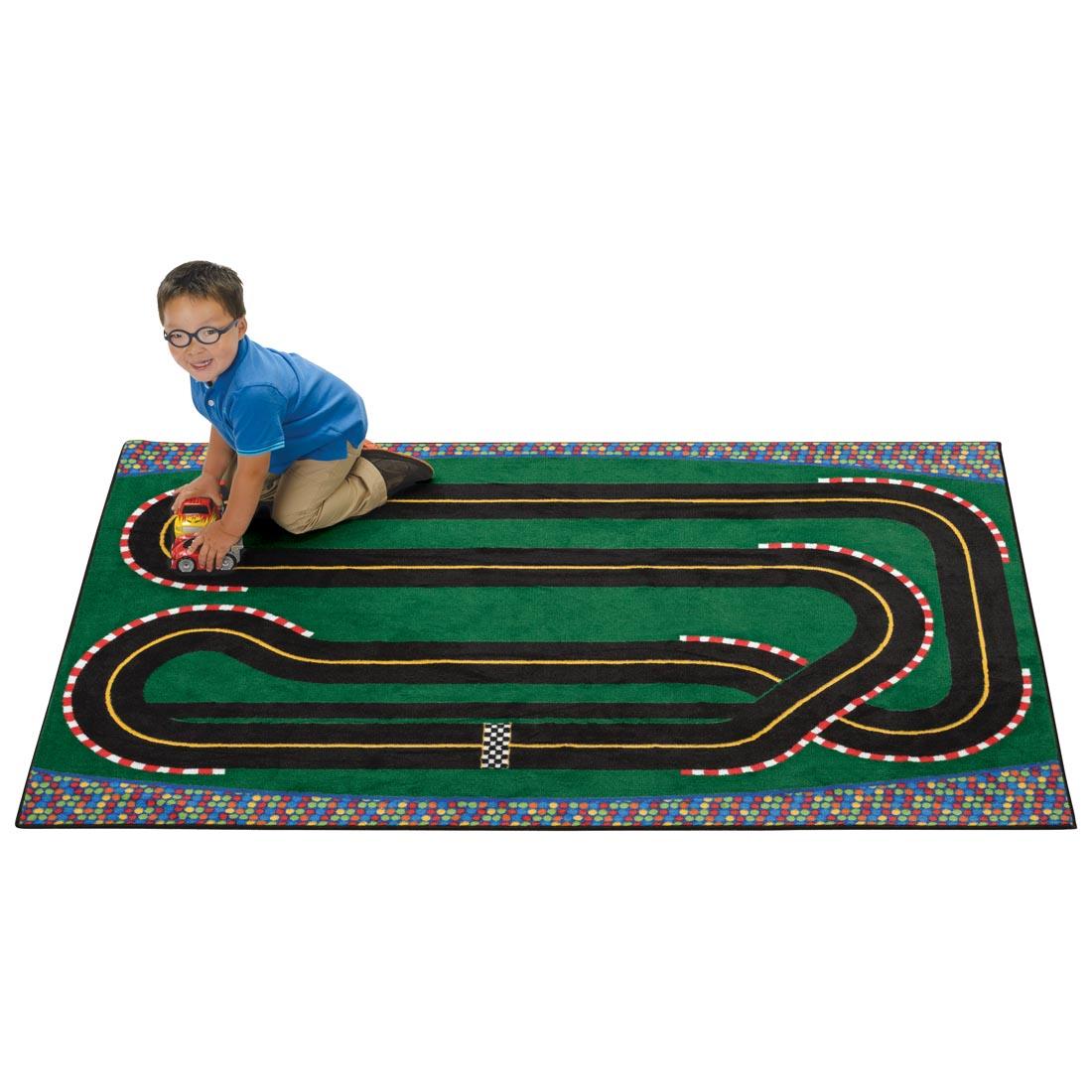 Super Speedway Racetrack Kids Value Rug by Carpets For Kids with a young boy kneeling on the rug, playing with a toy truck