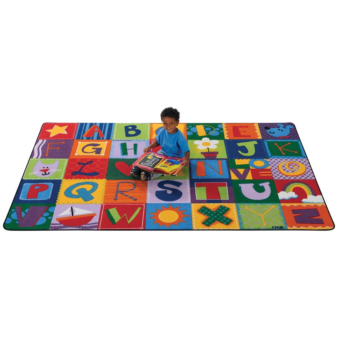 Child with a book sitting on the Toddler Alphabet Blocks Rug by Carpets For Kids