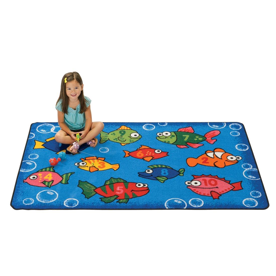 Fish Kids Value Rug by Carpets For Kids with a young girl sitting on the rug, holding a toy fishing rod