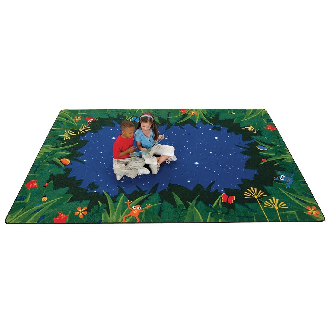 Children looking at a book while sitting on the Peaceful Tropical Night Rectangle Rug by Carpets For Kids