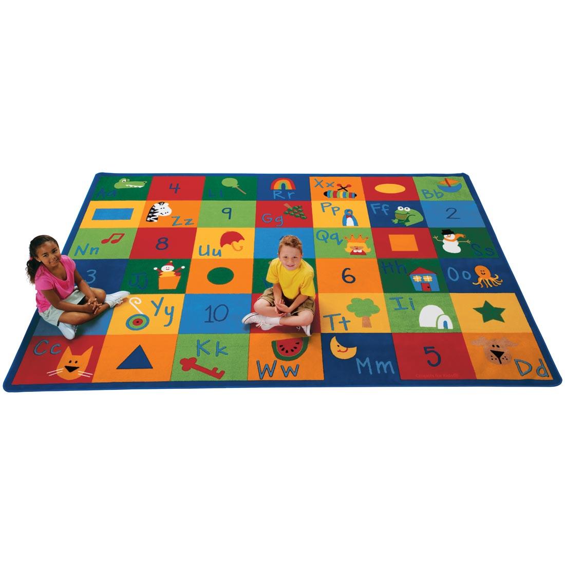 Learning Blocks Rectangle Rug by Carpets For Kids, with 2 young children sitting on the rug