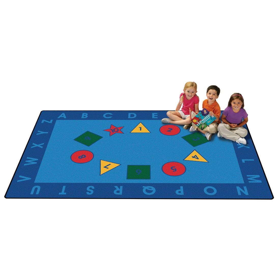 Early Learning Kids Value Plus Rug by Carpets For Kids, with 3 young children sitting on the rug, one is holding a book