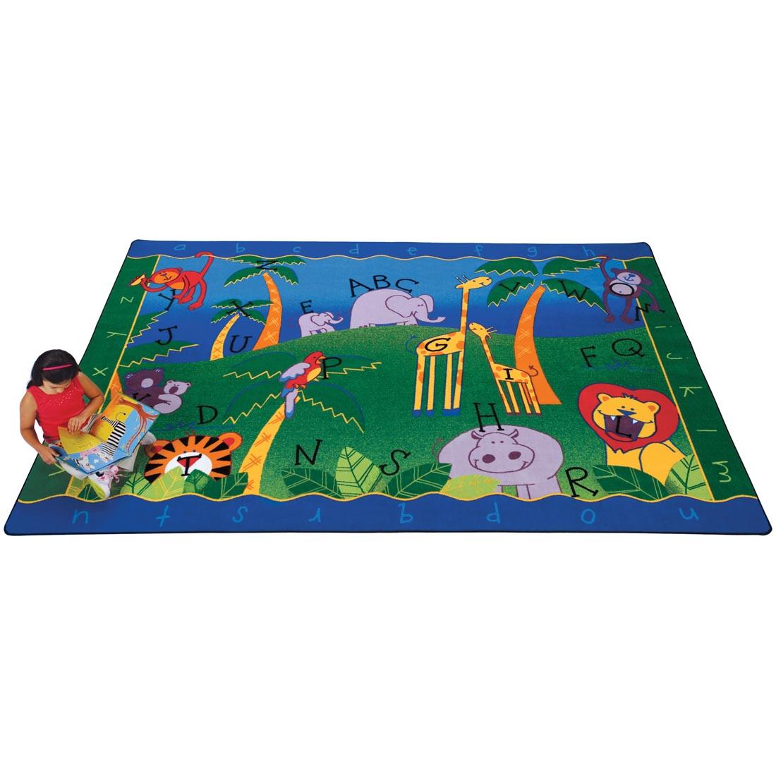 Child with a book sitting on the Alphabet Jungle Rug by Carpets For Kids
