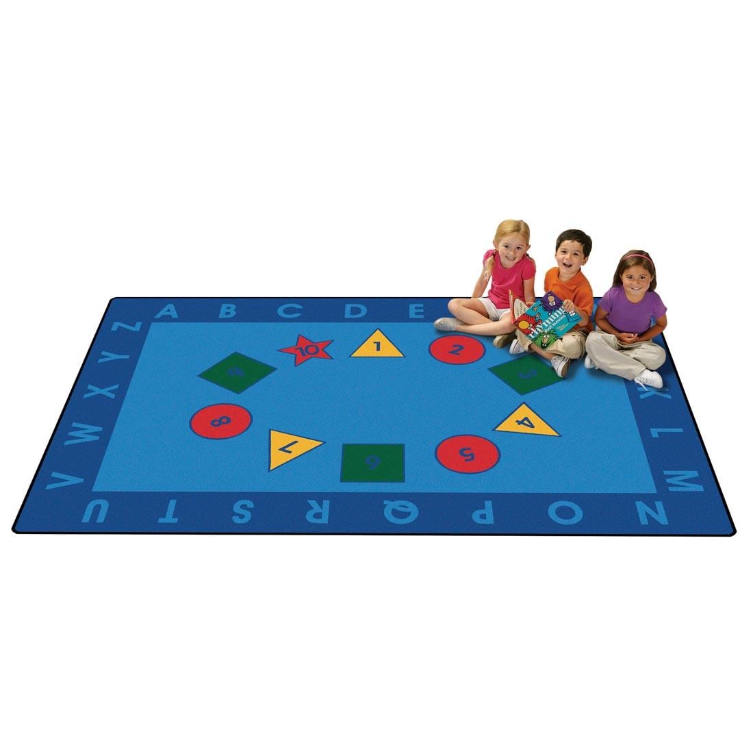 Early Learning Kids Value Plus Rug by Carpets For Kids, with 3 young children sitting on the rug, one is holding a book