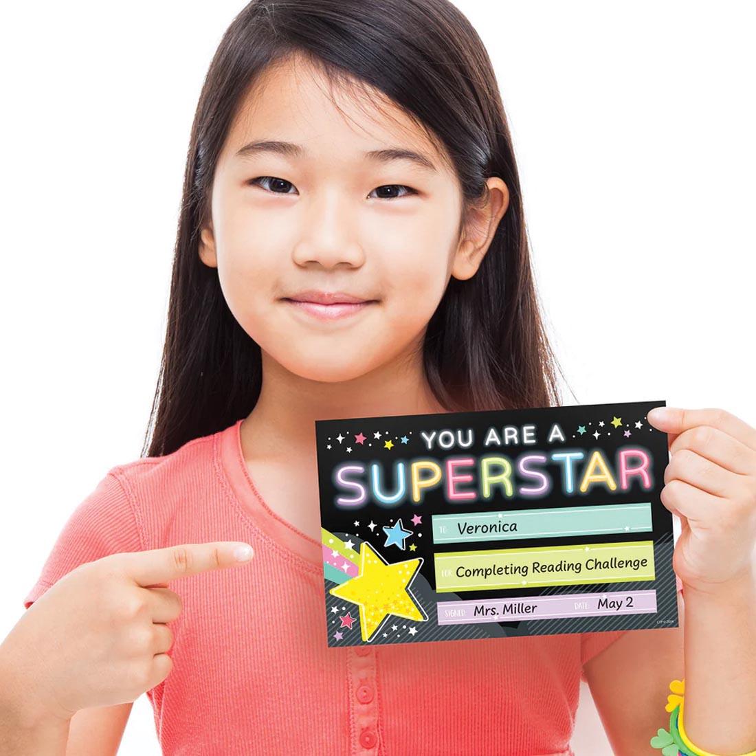 child holding their Superstar Award from the Star Bright collection by Creative Teaching Press