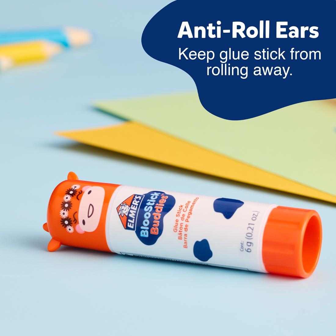 Elmer's BlooStick Buddies Washable Glue Stick laying on a table plus text Anti-Roll Ears Keep glue stick from rolling away.