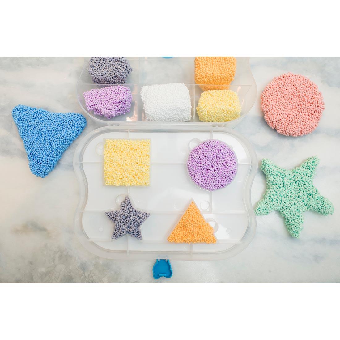 Several colors of Playfoam Modeling Material molded into various shapes, some in the mold outlines found in the package container
