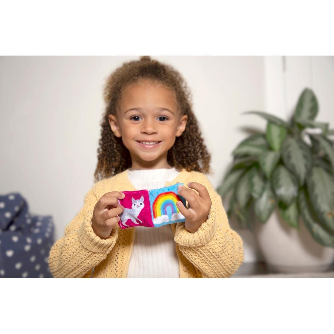 child holding up 2 bean bags, one with a picture of a cat, the other with a picture of a rainbow