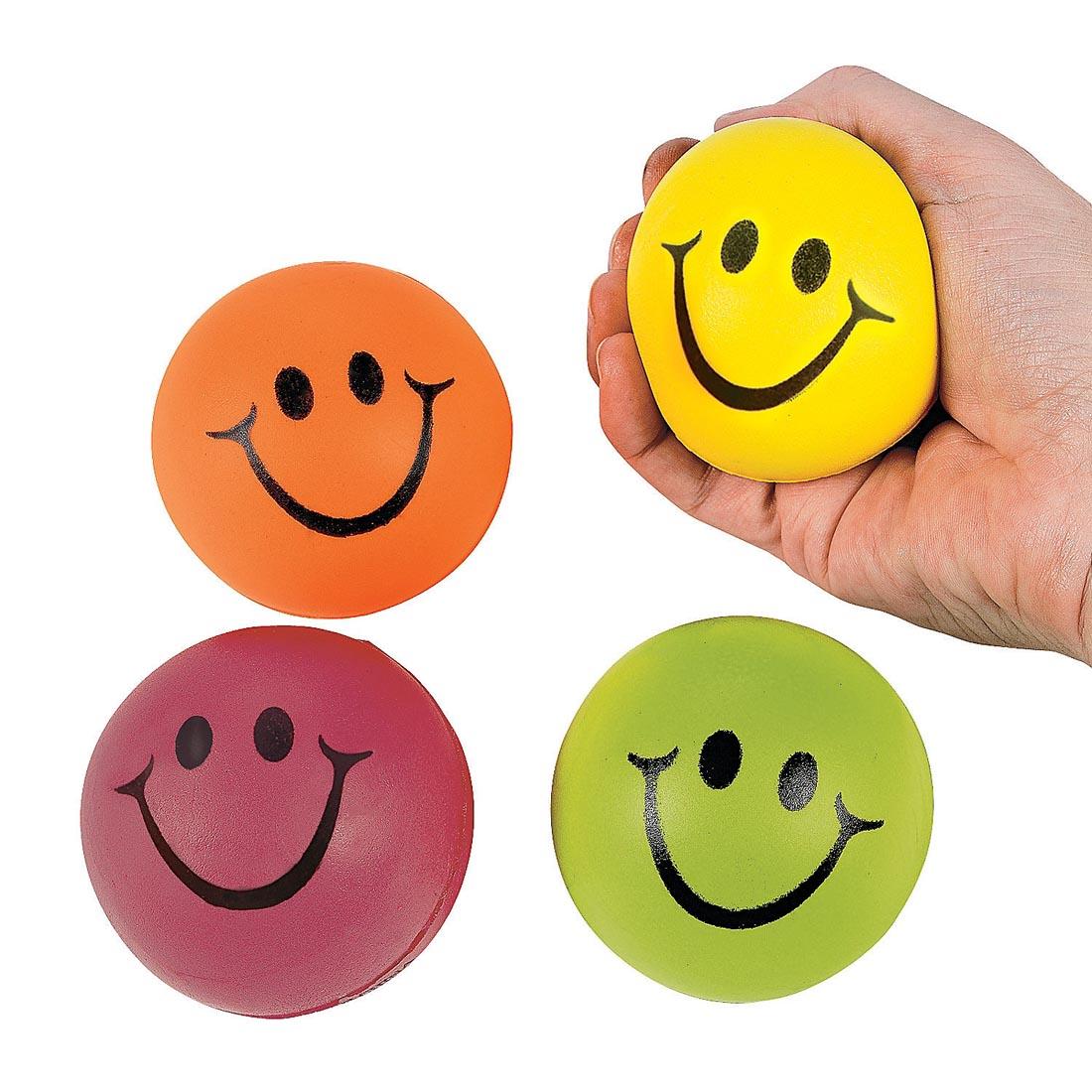 four Neon Smile Face Stress Balls by Fun Express with a hand squeezing one of them