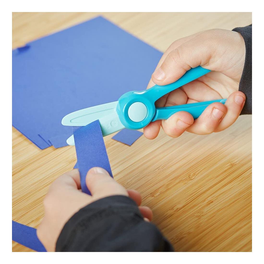 hands using Fiskars Starter Scissors to cut blue paper