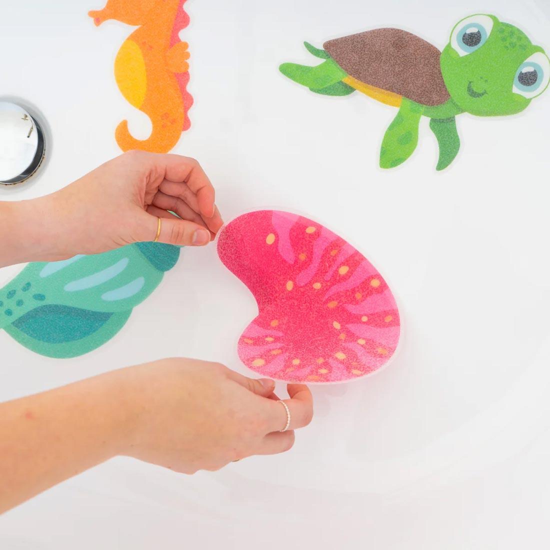 hands placing pieces of the Glow-In-The-Dark Guppy Grips Non-Slip Bathtub Stickies By Glo Pals