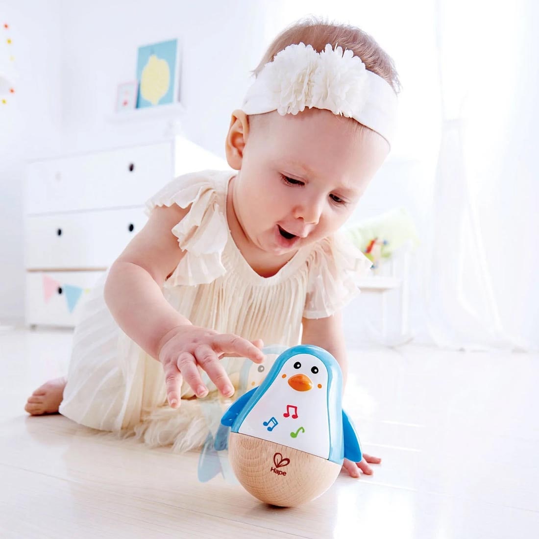 Child on the floor playing with the Penguin Musical Wobbler By Hape