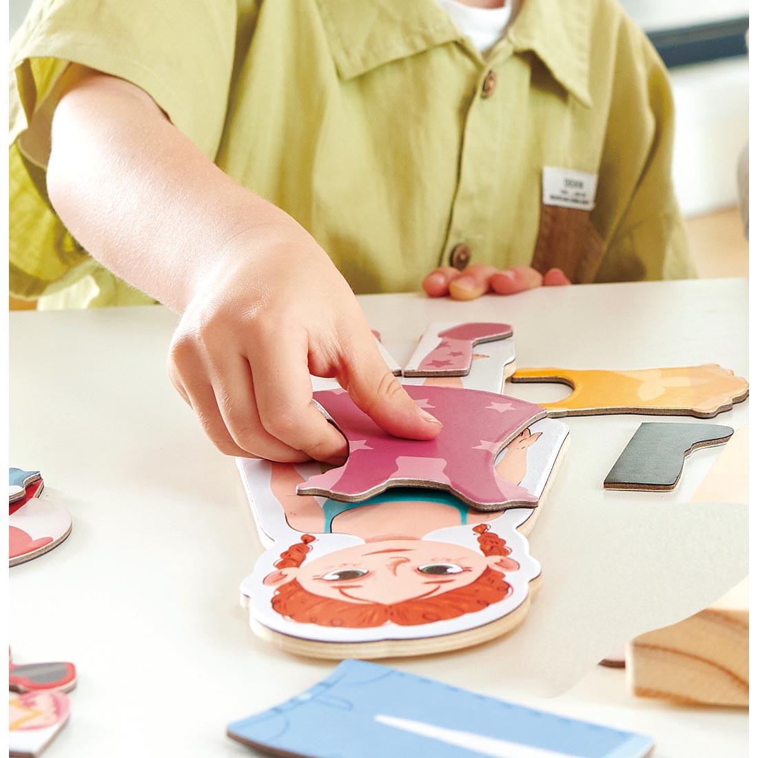 a hand placing a piece on the Dress-Up Magnetic Puzzle By Hape