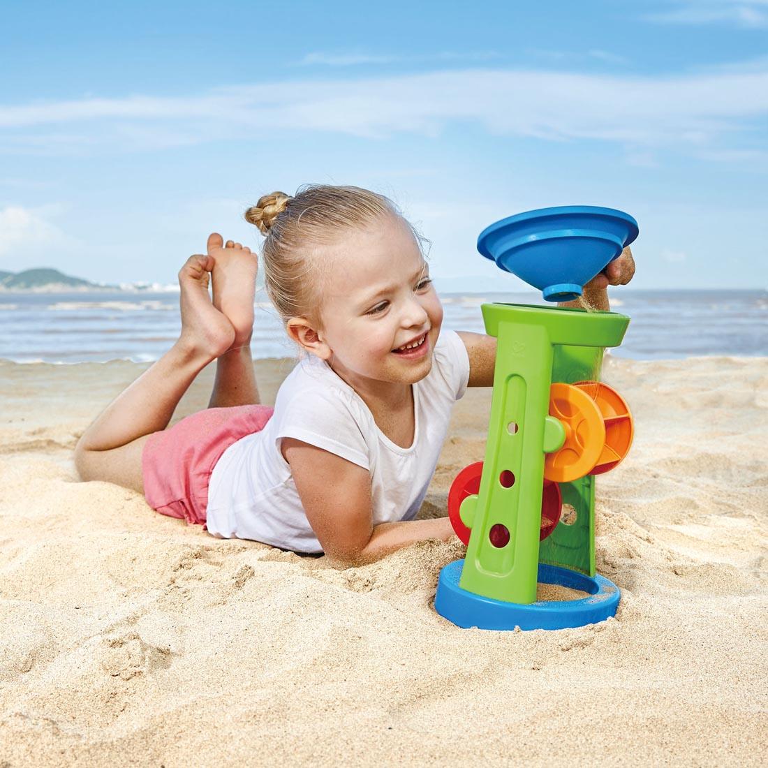 Child at the beach playing with the Double Sand And Water Wheel By Hape