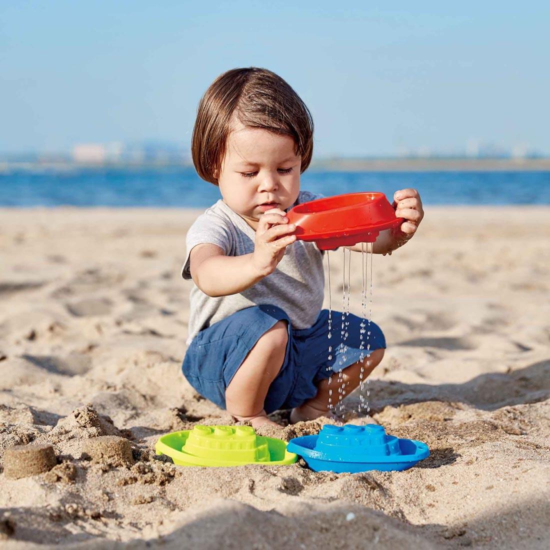Child at the beach playing with the Beach And Bath Boats By Hape