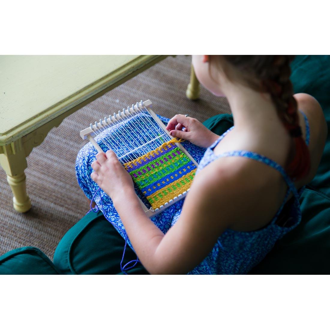girl using the Friendly Loom pegLoom as it rests in her lap, shown from over her left shoulder