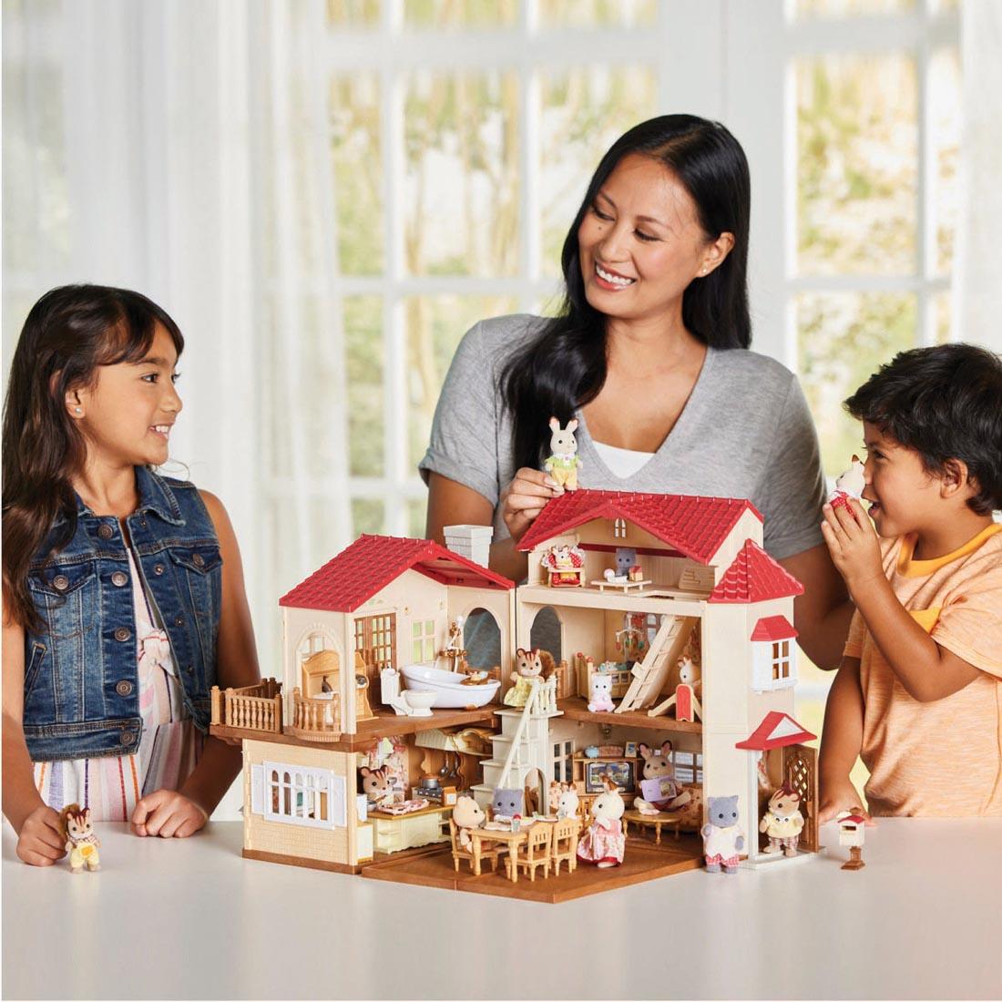 adult and 2 children playing with the Calico Critters Red Roof Country Home With Secret Attic Playroom