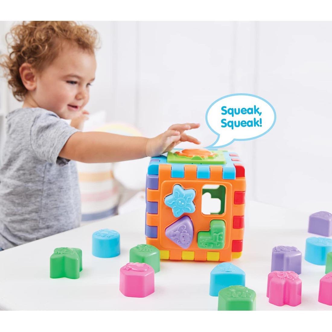 child pressing the button on the 2-In-1 Shape Sorter By Kidoozie with the text Squeak, Squeak!