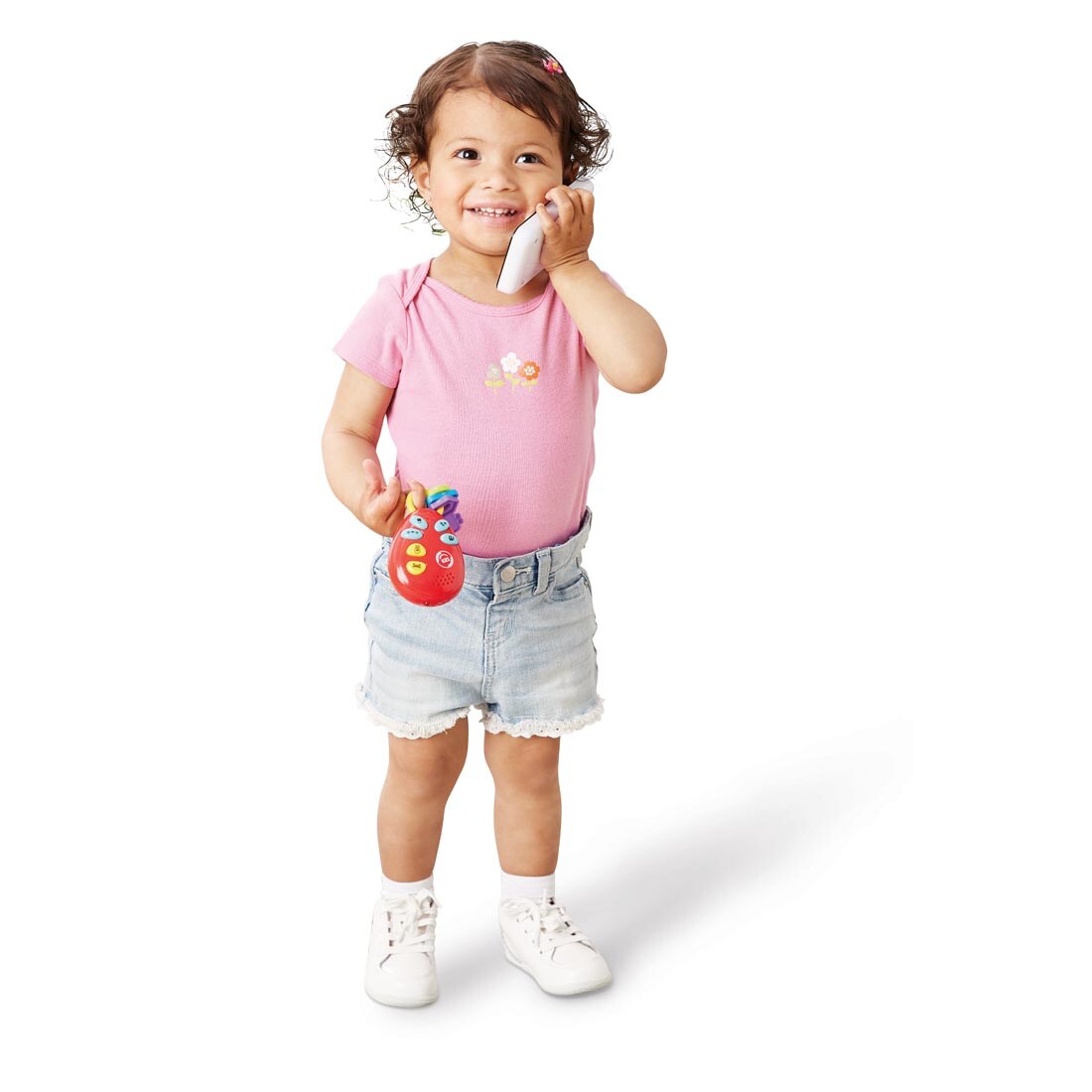 Young girl holding a toy phone to her ear and carrying a set of play keys, both toys from the Phone & Keys Combo Set By Kidoozie