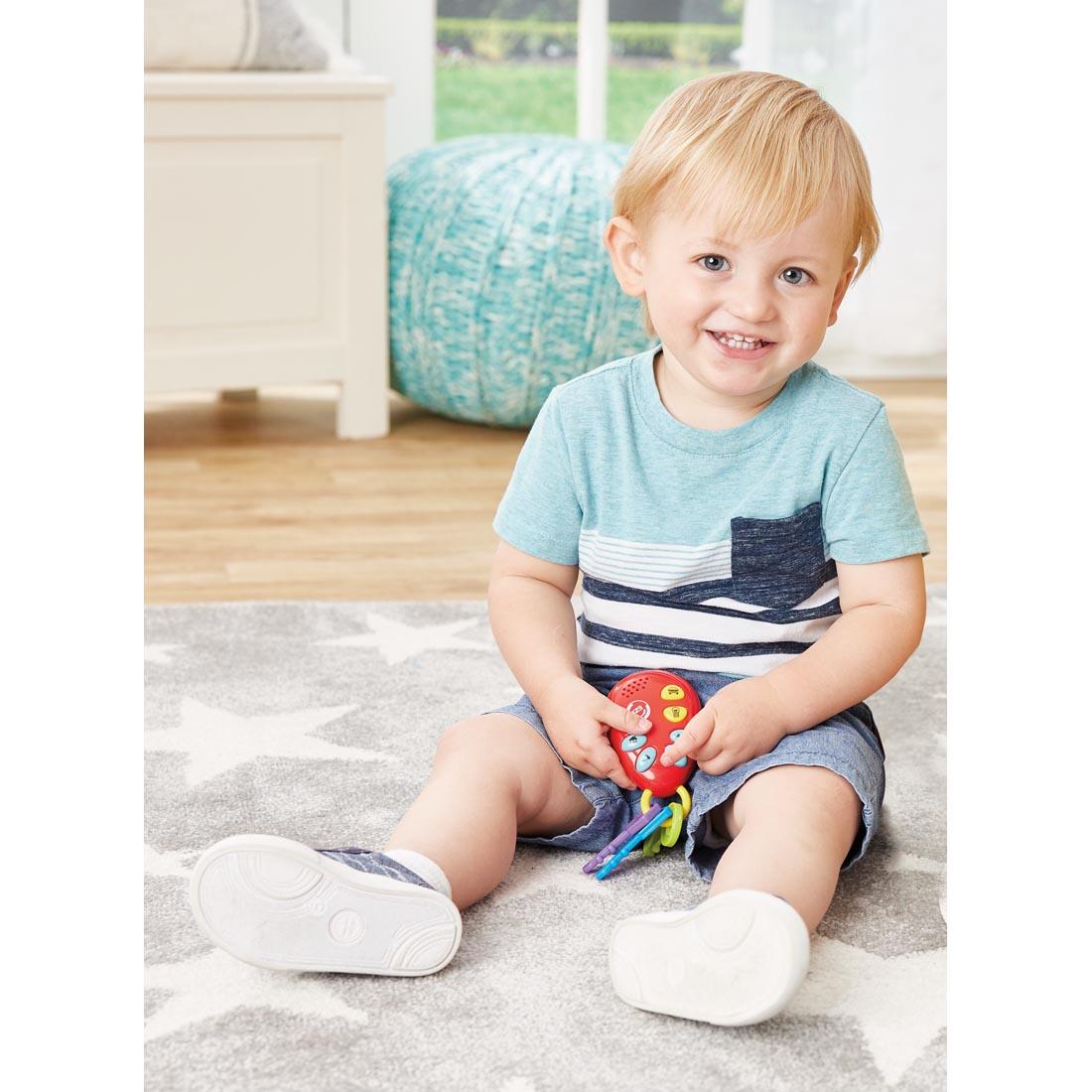 young child sitting on the floor holding the play keys from Phone & Keys Combo Set By Kidoozie