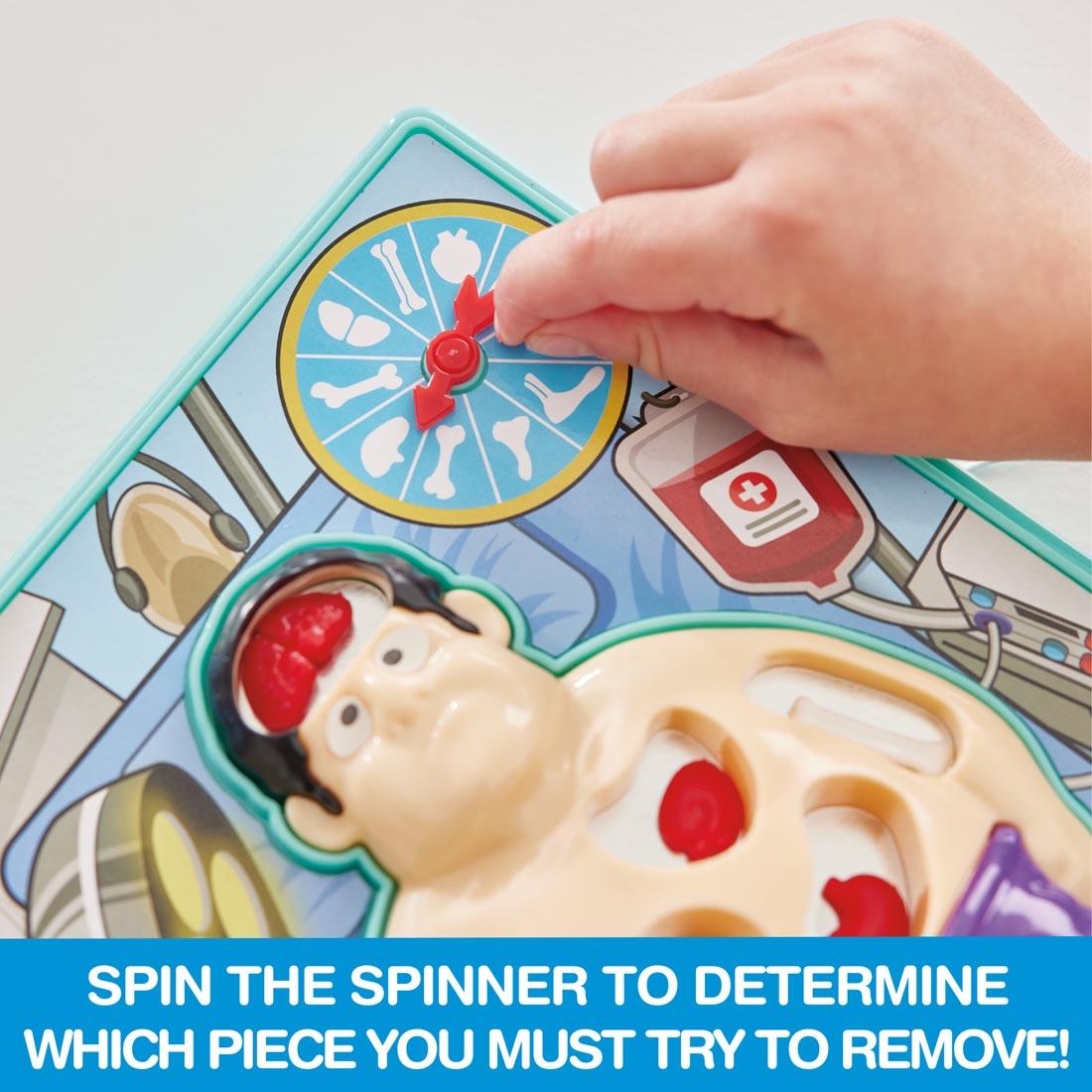 Hand touching spinner on Doctor's Dilemma game, with the words: Spin the spinner to determine which piece you must try to remove!