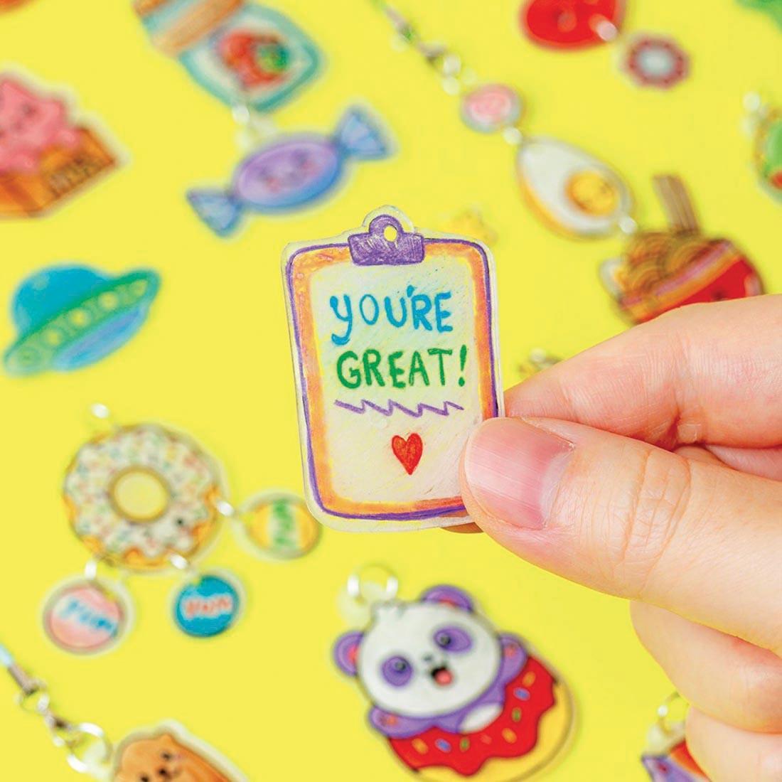 hand holding a charm made with Kawaii Style Color & Shrink Charms Book & Creative Kit By Klutz Press with other examples in the background