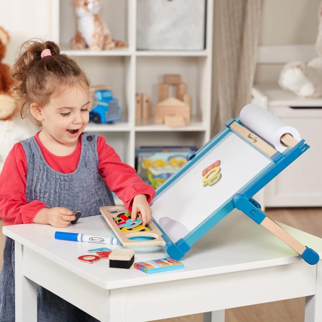 Child standing at a table playing with the Deluxe Double-Sided Tabletop Easel By Melissa & Doug