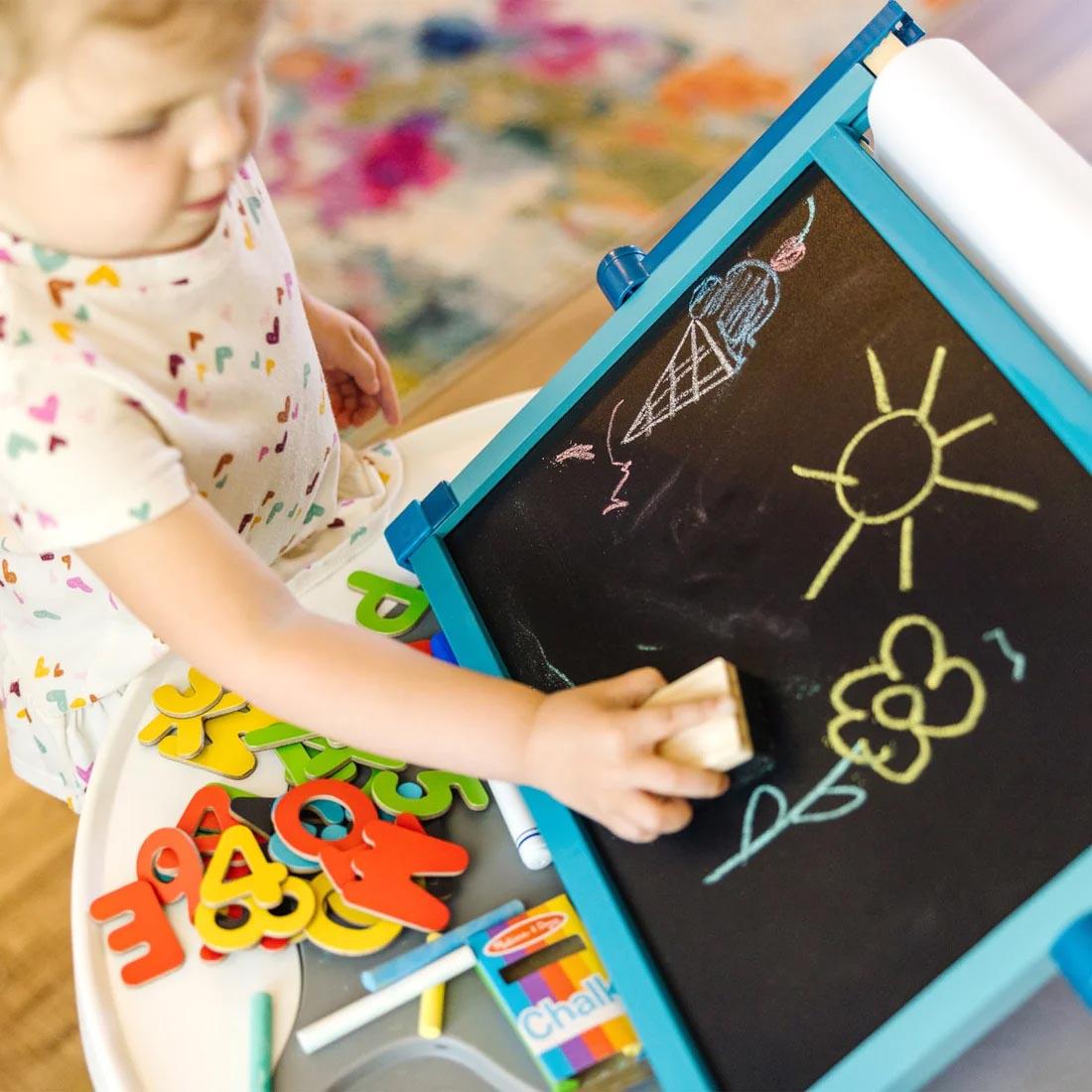 Child using an eraser on the Deluxe Double-Sided Tabletop Easel By Melissa & Doug