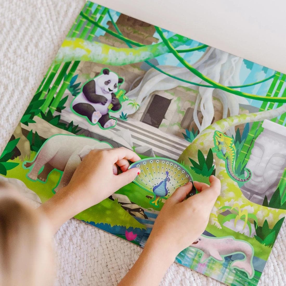 child's hands putting a sticker on one of the scenes from Jungle & Savanna Reusable Sticker Pad By Melissa & Doug