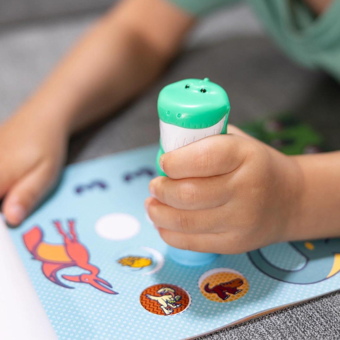hands using the stamper that comes with the Dinosaur Sticker Wow! Set By Melissa & Doug