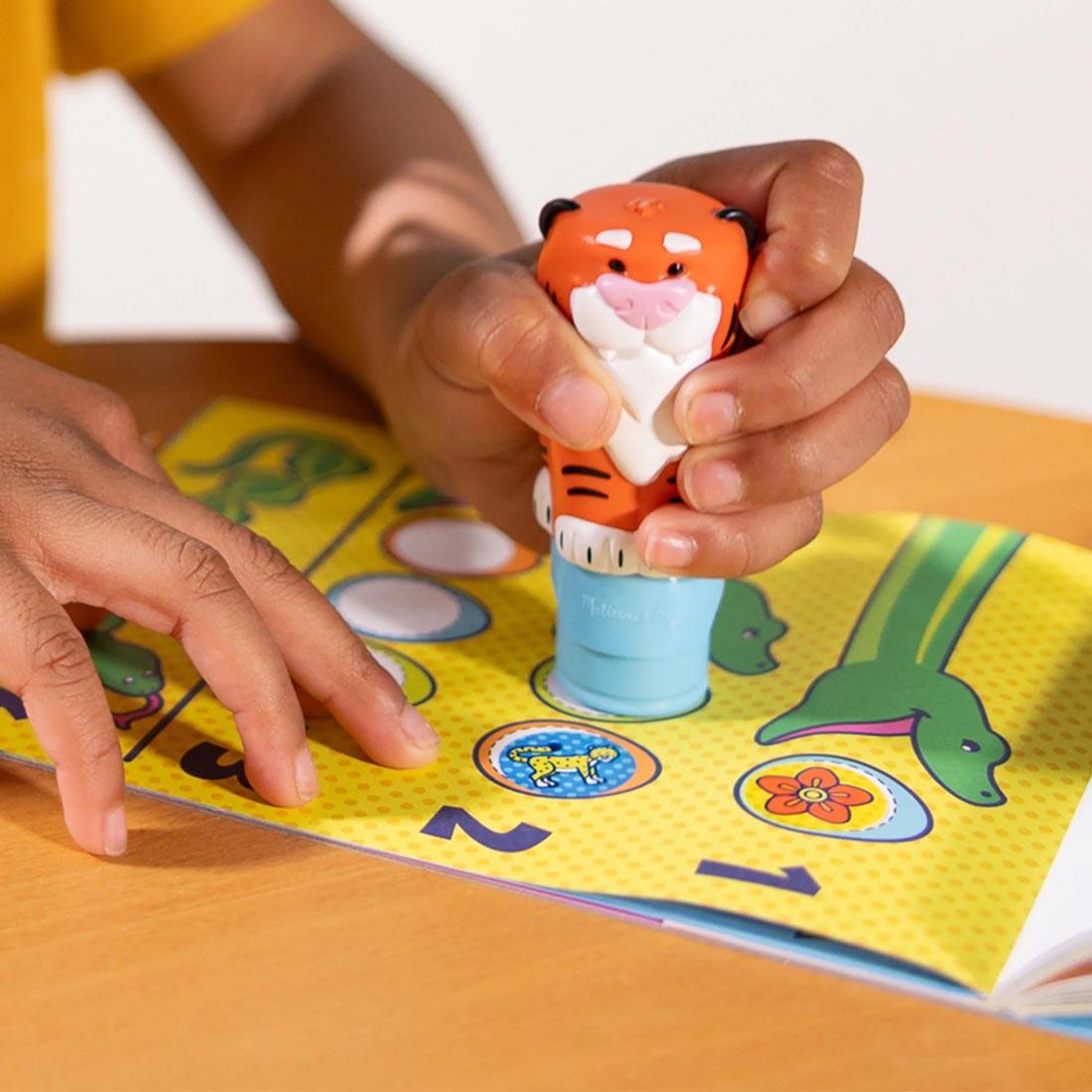 child's hands using the stamper from the Tiger Sticker Wow! Set By Melissa & Doug