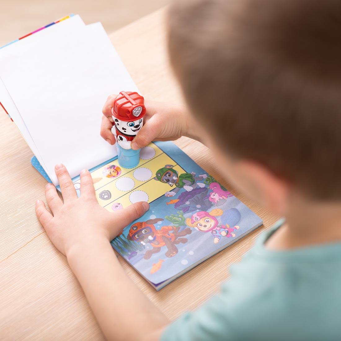 Boy using Paw Patrol Marshall Sticker Wow! stamper to place stickers in the included activity book