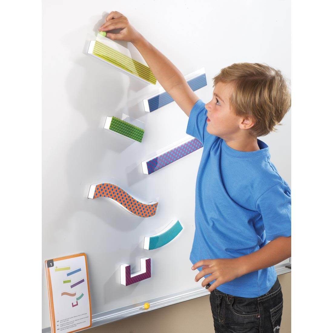 child placing a marble at the top of a Tumble Trax Magnetic Marble Run that is attached to a whiteboard