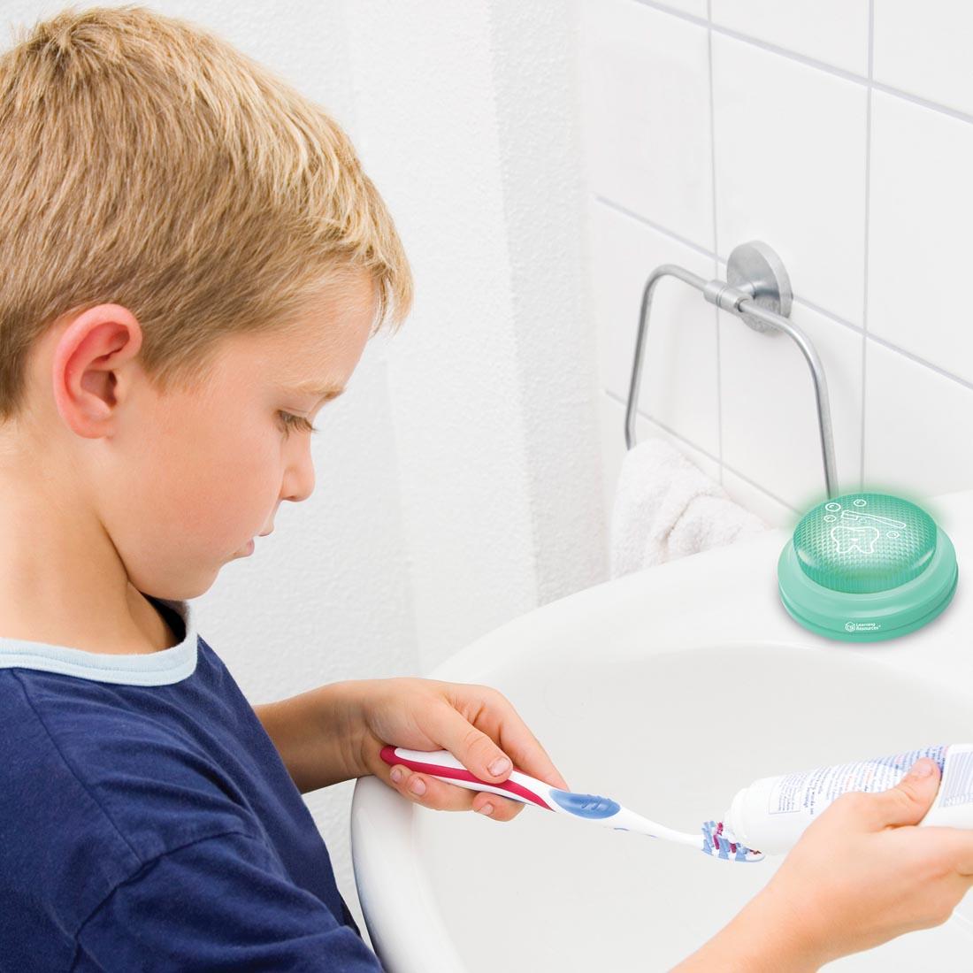 child at the sink holding toothbrush and toothpaste with the 2-Minute Toothbrushing Timer By Learning Resources nearby