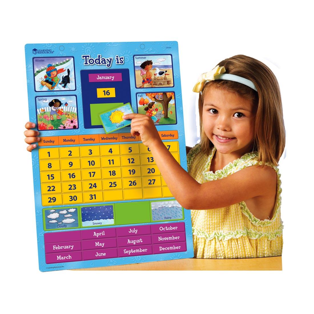 child holding a Magnetic Learning Calendar with spots for seasons, weather, months and days