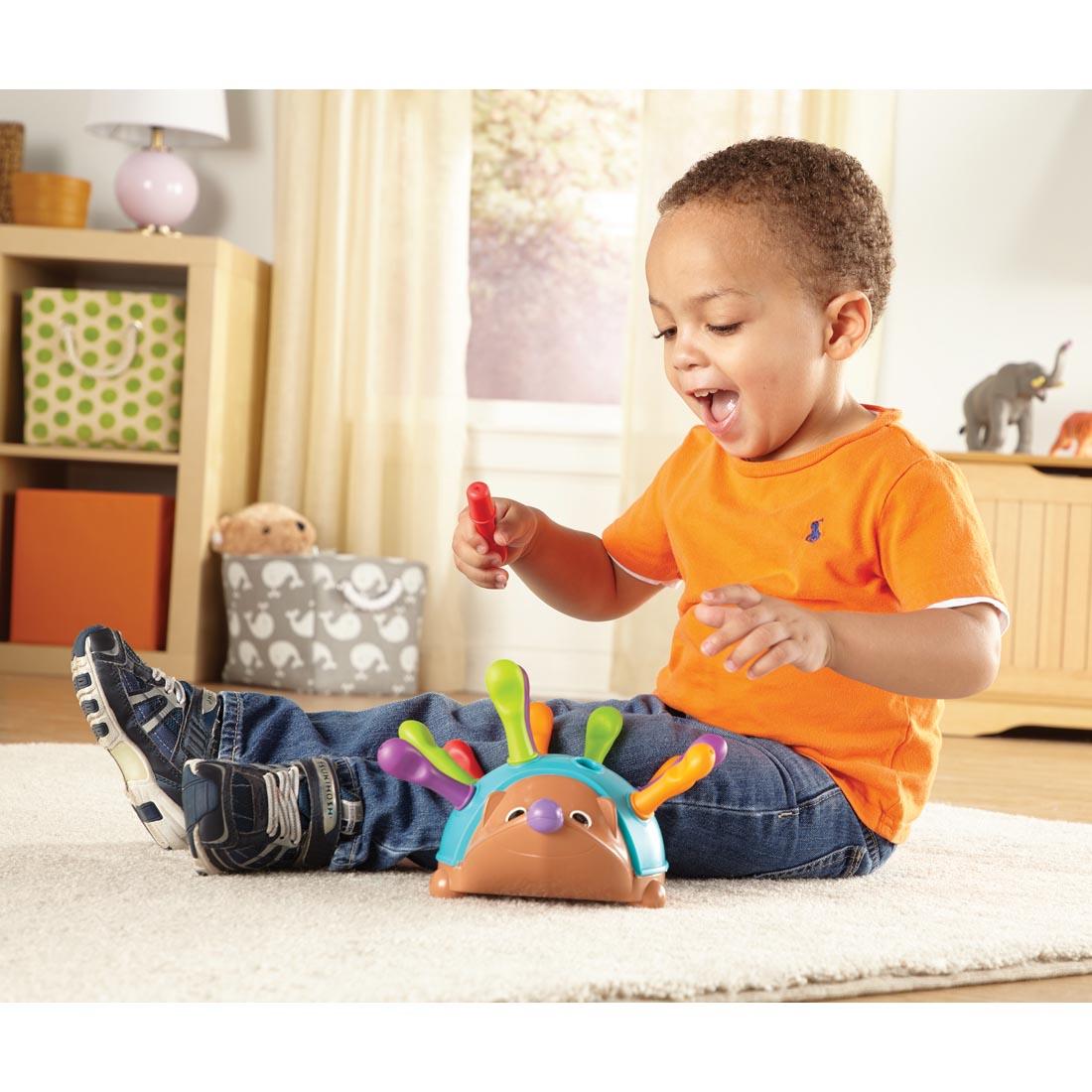 child on the floor playing with Spike the Hedgehog, fitting plastic spikes into the holes on its back