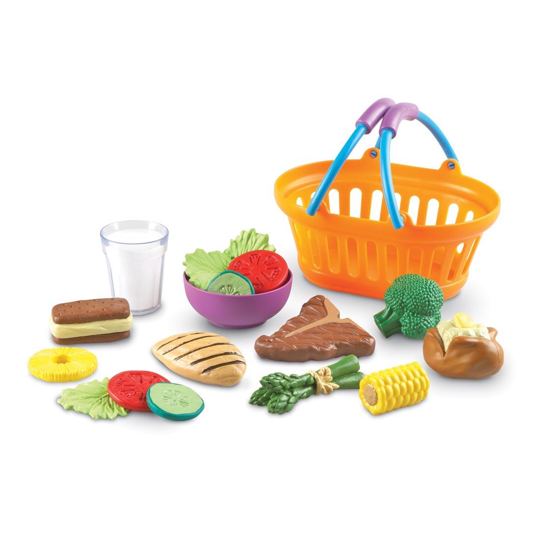 plastic basket next to play food including bowl of salad, grilled chicken breast, baked potato with butter and more