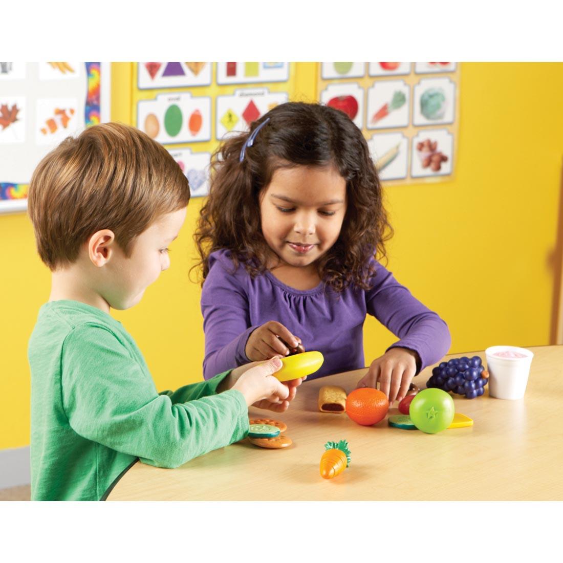 children playing with play food including granola bar, banana, carrot, grapes and more