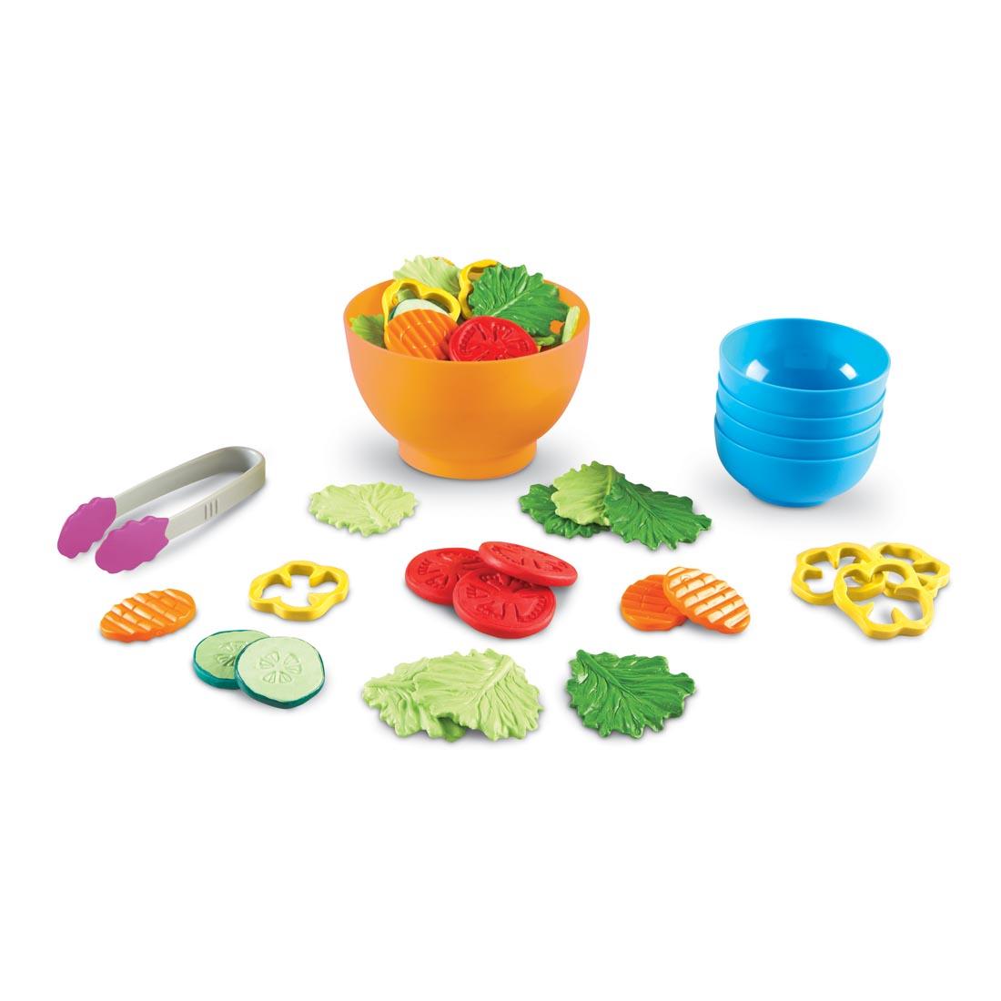 tongs and bowls with play food such as lettuce, sliced tomatoes, sliced carrots, sliced cucumbers and more