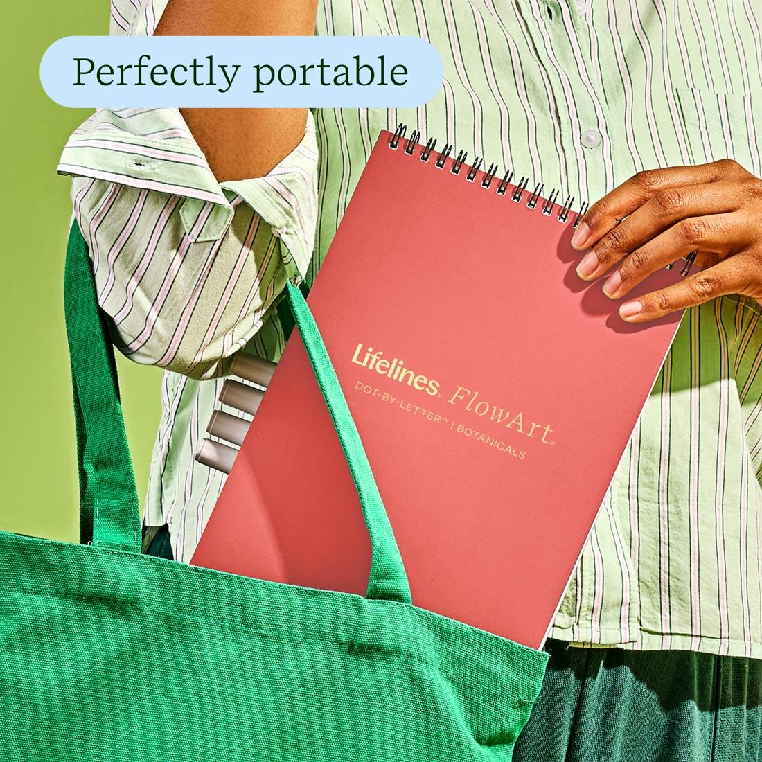 close up of a hand putting FlowArt Dot-By-Letter Botanicals pad by Lifelines in a bag, with the words: Perfectly portable