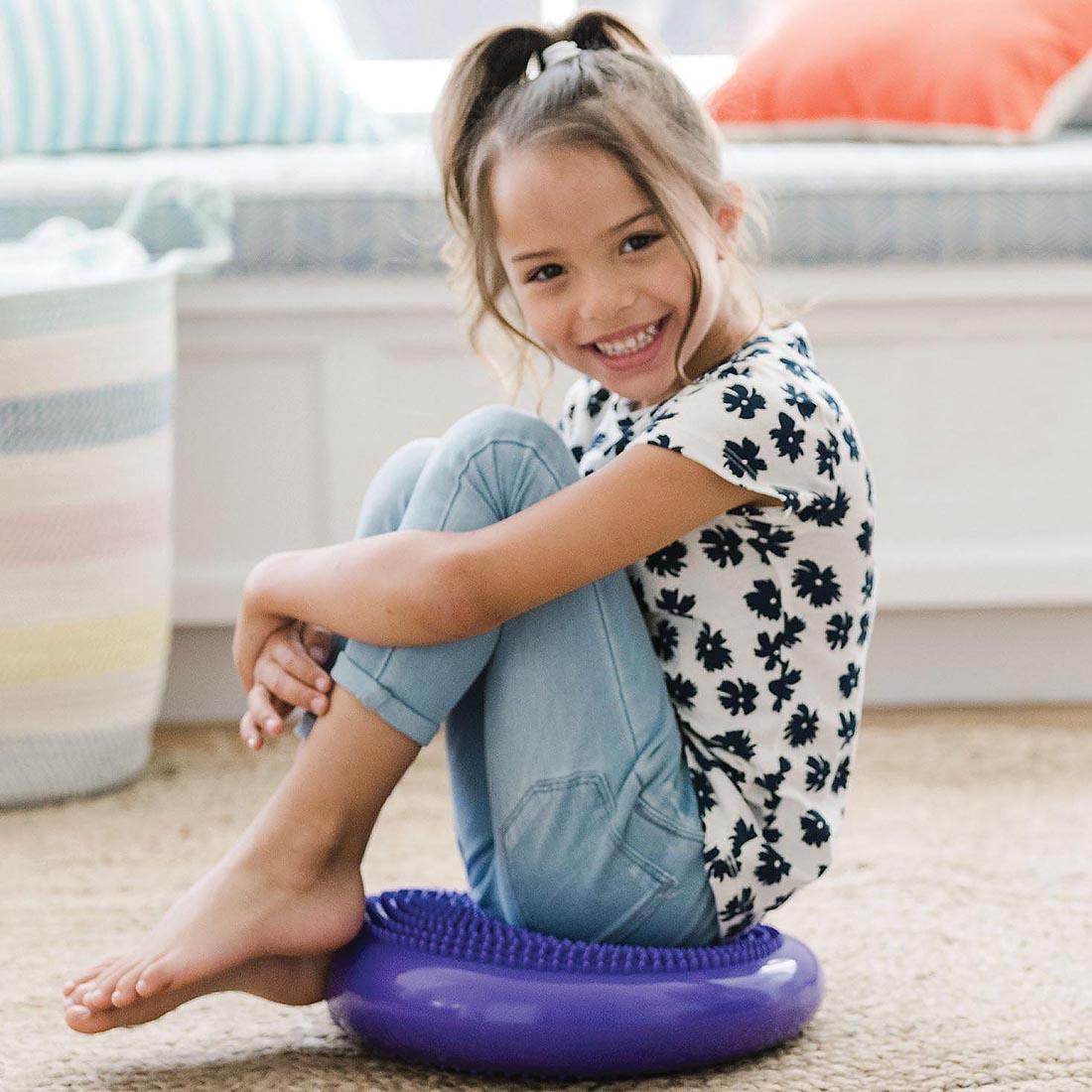 child using the Sensory Genius Wobble Cushion By Mindware on the floor
